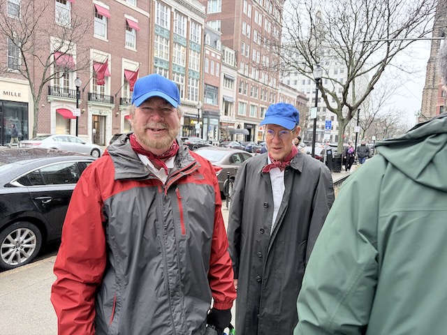 View of Newbury Street with two people in gray and red raincoats and blue hats on the sidewalk.